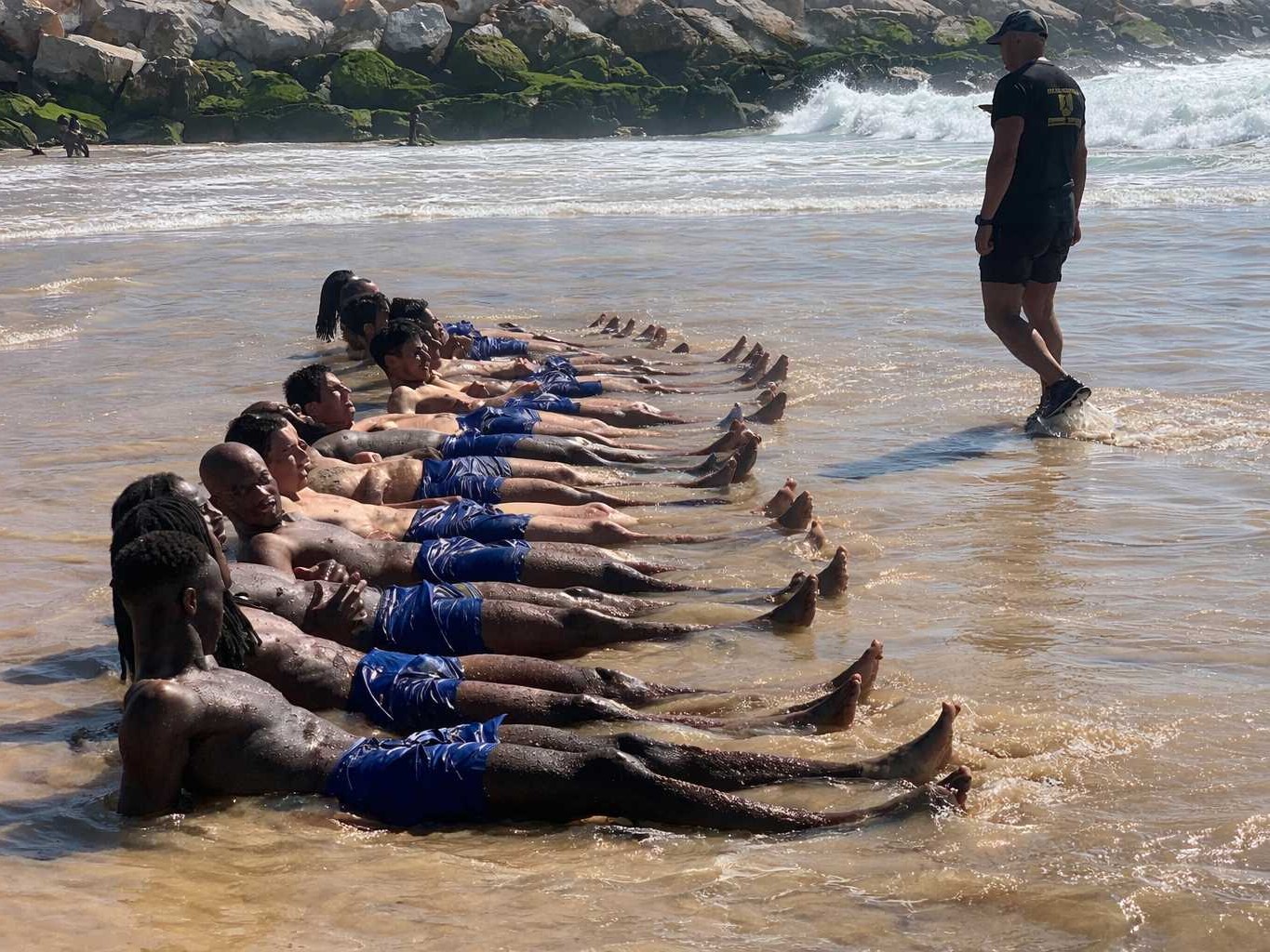 Equipa de clube desportivo a fazer desafio em grupo de team building no mar com instrutor militar a observar
